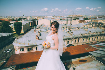 Fototapeta na wymiar Happy bride with a wedding bouquet on the roof of the city