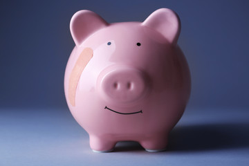 Piggy Bank with adhesive bandage on grey background