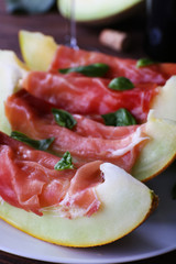Melon with prosciutto of Parma ham on wooden table, closeup