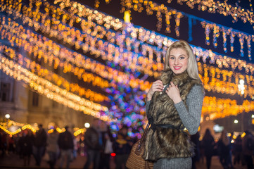 Obraz na płótnie Canvas Portrait of young beautiful woman with long fair hair outdoor in cold winter evening. Beautiful blonde girl in winter clothes with xmas lights in background. Beautiful woman smiling in winter scenery