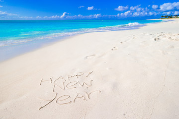 Fototapeta na wymiar Happy New Year written on beach white sand with red Santa hat