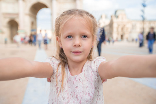 Adorable little girl taking selfie with mobile phone outdoors in Paris