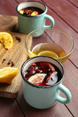 Mulled wine in a mug with citruses on wooden background, close up