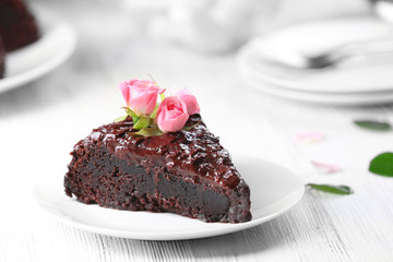 Piece of chocolate cake decorated with flowers on white wooden table
