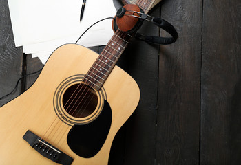 Fototapeta premium Acoustic guitar, headphones, musical notes and white papers on wooden background, close up