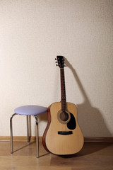 Fototapeta na wymiar Acoustic guitar propped on wall with stool in the room