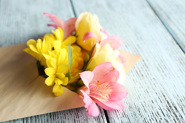 Fresh bouquet of flowers in envelope on wooden background