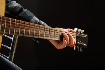 Musician plays guitar on black background, close up