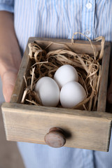 Eggs in basket in women hands on wooden background