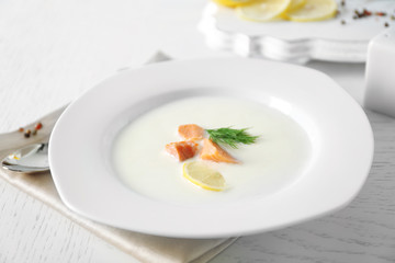 Delicious cream soup with fish and sliced lemon on white table in the restaurant
