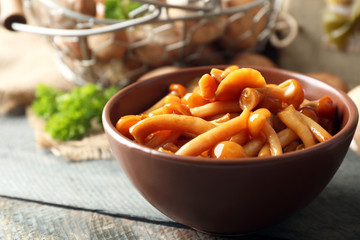 Delicious marinated mushrooms in bowl on wooden background