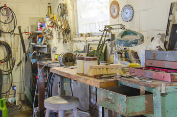 A very messy workshop with a huge variety of tools, work bench, lamp and much more.