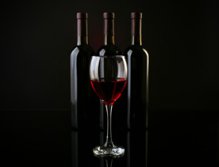 Wine glass against bottles in a row on dark red background, close up