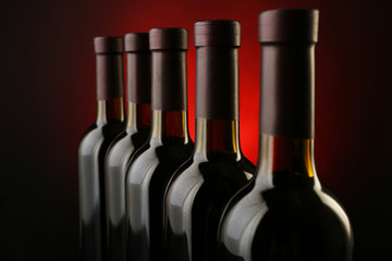 Wine bottles in a row on dark red background, close up