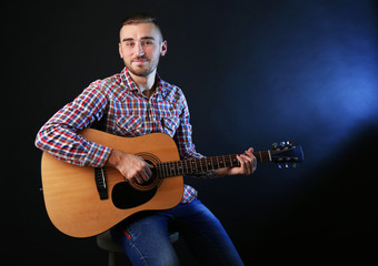 Obraz premium Young man playing on guitar on dark background