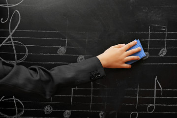 View on schoolboy's hand cleaning the blackboard with musical notes, close-up