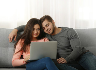 Young happy couple using laptop at home on light background