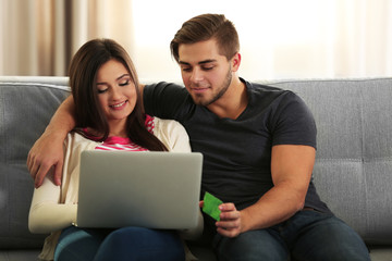 Young happy couple using credit card with laptop at home on light background