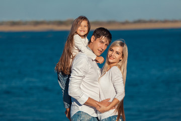 Fototapeta na wymiar Young family in blue jeans hugging on the background of water