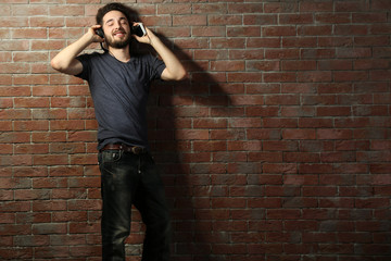 Young handsome man listening music with headphones on brick wall background