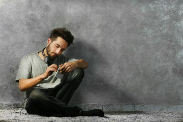 Young bearded man listening music with headphones on grey wall background