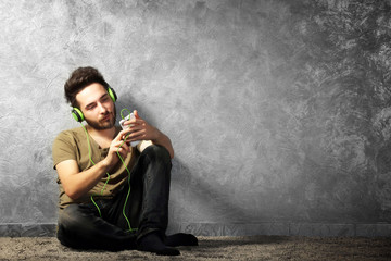 Young bearded man listens music with headphones sitting on grey wall background