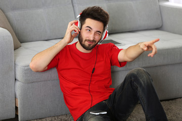 Handsome man listens music with headphones on the floor against grey sofa in the room