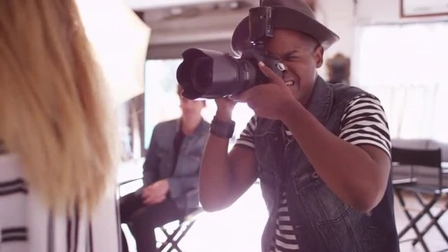 Black fashion photographer shooting photos on studio set with team of assistants behind him