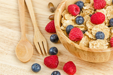 Bowl of cereals with raspberries and blueberrys on a wooden table.