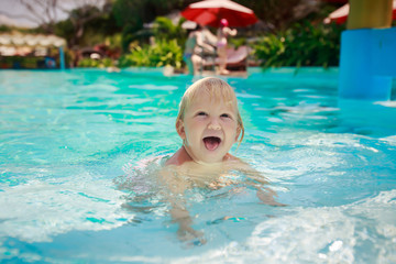 Fototapeta na wymiar small blonde girl stands screws up eyes in shallow pool water