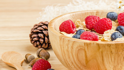 Bowl of cereals with raspberries and blueberrys on a wooden table.