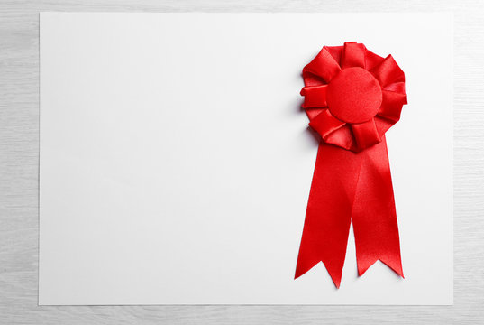 Award ribbon on white paper sheet, on wooden background