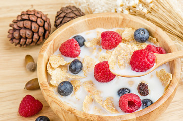 Bowl of cereals with raspberries and blueberrys on a wooden table.