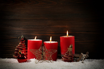 Three red candles, toys, star and sledge in a snow over wooden background, still life