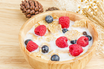 Bowl of cereals with raspberries and blueberrys on a wooden table.