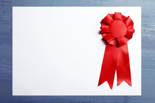 Award ribbon on white paper sheet, on wooden background