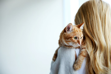 Young woman holds red cat in hands, close up, back view