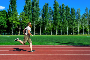 Fototapeta premium Bearded man running at stadium wearing sunglasses. Concept of persistence, healthy activity, goals achieving
