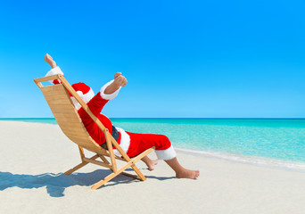 Christmas Santa Claus enjoy sun on deckchair at sandy beach