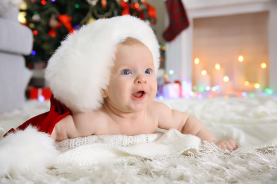 Naked baby in red hat on the floor in the decorated Christmas room