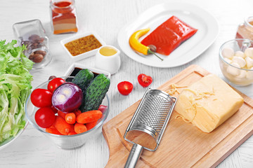 Kitchen utensils and ingredients for salad on table, on light background