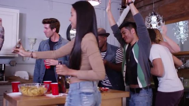 Group of young fun loving young mixed race friends partying and dancing in kitchen