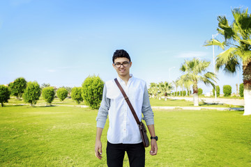 Portrait of a happy young man standing outdoors with small bag.