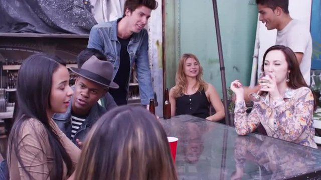 Mixed race group of hipster friends talking and laughing in urban backyard party