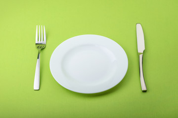 Empty plate, fork and knife on green background