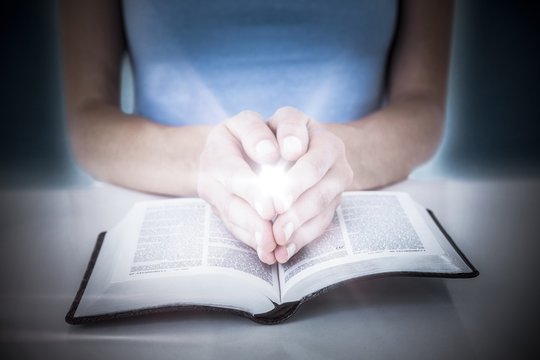 Composite image of woman praying while reading bible