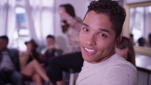 Portrait of Handsome young mixed race hipster man smiling at camera with group of friends partying in background