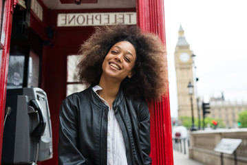 Obraz premium Smiling portrait of young woman close to red telephone box in London.
