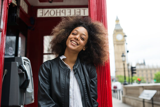 Smiling portrait of young woman close to red telephone box in London.