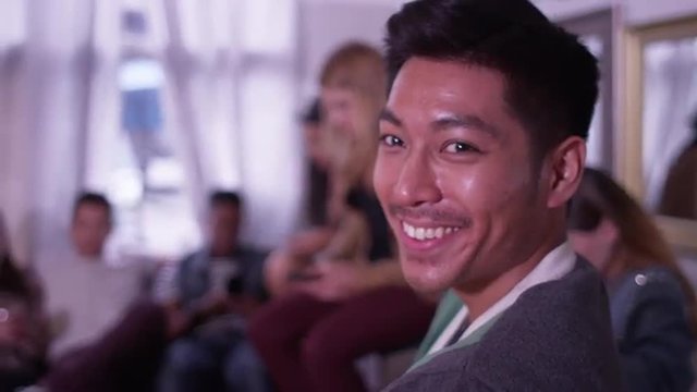 Portrait of Handsome young asian hipster man smiling and laughing with group of friends partying in background